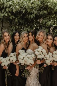 Modern Moody El Chorro Wedding - Scottsdale wedding design with white flowers and desert mountain views. Long stem white rose bouquet. Bridesmaids wore black dresses and carried white flower bouquets. Floral columns were featured in the ceremony. The reception had candles and bud vases with white flowers. Black signs and accents were used in the ceremony and reception. Photos by Emerald AZ.