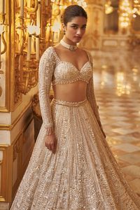 This lehenga set features delicate embroidery in ivory and gold sequin in a geometric pattern,. The full sleeves blouse has a plunging neckline and shows pearl and crystal tassels at the waist and wrist. It is paired with a matching four sided embroidered dupatta.From Seema Gujral's Inara collection. DELIVERY TIMEPlease allow 8-12 weeks for your outfit to arrive. FABRIC DETAILSNet Professional cleaning only.