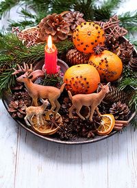 Winter altar for Yule sabbat. candle, toy deer family, cinnamon, nuts, cones, decorated oranges, fir branches in plate on wooden table. Christmas and new year concept. Festive winter season