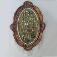 Dieser verstellbare hängende Schmuckhalter eignet sich perfekt für die Aufbewahrung von Ohrringen, Broschen, Ringen, Halsketten und vielem mehr. Es ist auch eine Retro-Wandkunst, was den Schmuck und den Rahmen zu einer lustigen und interessanten Wanddekoration macht. Ideal für kleine Räume oder Häuser mit begrenztem Platz auf dem Schreibtisch. Harz-Rahmen: Es ist aus Harz gefertigt und mit einer dekorativen Perlenfranse verziert, mit einem Samtkern, der dem Produkt einen raffinierten Retro-Look verleiht. Das offene Design des Kerns ermöglicht es Ihnen, Ihren Schmuck frei aufzuhängen und Ihr eigenes Stillayout zu erstellen. Kunststoffrahmen: Die Fassung besteht aus Kunststoff, der Kern ist mit Zierperlen eingelegt, und es hat einen dunkelgrünen Samt als Untergrund. Kommt mit 5 kleinen Perle