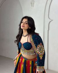 Exude charm and grace with this stunning multi-colored lehenga featuring intricate embroidery, mirror work, and shell embellishments. The deep blue blouse adds a touch of elegance, while the colorful skirt brings a burst of festive energy. Perfect for Navratri, wedding functions, or any traditional celebration, this outfit is sure to turn heads and make you feel effortlessly chic.