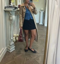 Are you looking for some fall outfit ideas? Here is a trendy outfit idea pairing a trench coat, denim vest, mini skirt, and mary jane flats. Add a pop of fall color with a handbag! 