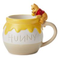 Start any day with a smackerel of sweetness with this cute Winnie the Pooh sculpted mug. Ceramic cup of a hunny pot features Pooh sitting on the rim, ready to swipe a pawful of honey. Perfect for cocoa, coffee and hot tea (especially when you add honey), this 17-ounce cup makes a delightful gift for a Winnie the Pooh fan. | Sculpted ceramic mug features Disney Winnie the Pooh sitting on a honey pot. | On mug: HUNNY. | Ceramic. | Dishwasher safe. Do not microwave. | Holds 17 oz. | 5.5" W x 4.75"