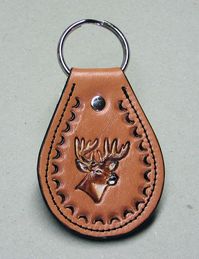 Hand tooled and painted cowhide leather key fob with deer head design. Fob measures approximately 4" long X 2-1/4" at the widest part. It is lined with pigskin leather and is glued and sewn. Edges are trimmed so it isn't sharp, dyed, and burnished smooth.  Fob is attached to an 1-1/4" nickel plated split key ring with a double cap rivet. Overall length is approximately 4" long and 2-1/4" wide at the widest part.