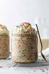 Birthday cake overnight oats in a jar, topped with whipped cream and sprinkles.