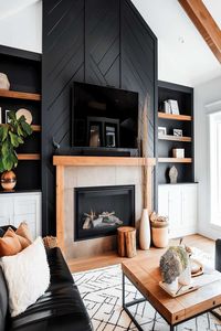 This modern living room features a striking black fireplace wall complemented by wooden accents, creating a cozy and stylish space. View the article for more inspiration and follow us for the latest design trends!