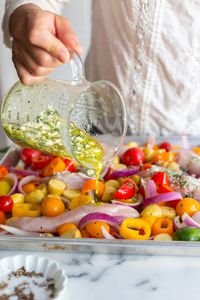 Adding marinade to the Herby Feta Lemon Chicken and Veggie Sheet Pan Dinner recipe by Baking The Goods