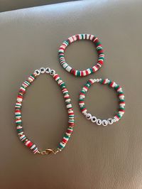 This is a preppy Christmas set with a plain red, white, and green bracelet, a red, white, and green pearled bracelet with the words "jolly" on it, and a red, white, and green necklace with the words "Xmas" on it with golden in between.