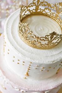 A beautiful two tiered princess party cake with pink and white buttercream, gold sugar pearls, and a gold princess crown cake topper. See more inspiration for your own princess party!