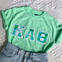 These classic and vintage-style letters are perfect for new and seasoned sorority women alike! Features double-stitched modern marbled, green geode letters on a stark white background attached to a comfortable unisex mint green tee. This seller is licensed with Affinity Licensing and Direct Licensing to ensure a verified, quality product.  Care Instructions: Machine wash cold, inside out; Tumble dry low; Low iron as needed