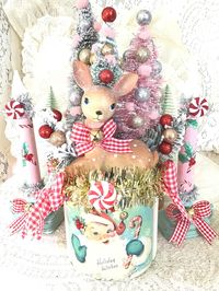 This adorable and one of a kind vintage Christmas Deer jar assemblage would make a welcome addition to your retro style and vintage style farmhouse Christmas decor!  Meticulously handcrafted baby Christmas Deer with decorated bottle brush tree diorama sets permanently attached to a glass canister jar painted with layers of my custom made chalk paint... This beautiful piece features a retro style Santa on the front and vintage Merry Christmas tag on the back, images applied using my special decoupage technique and adorned with sparkling rhinestone accents. The top of the jar features vintage style metallic gold tinsel garland and adorable and cute as can be red and white gingham bows with jingle bells and sweet little faux Christmas candies.  Absolutely adorable in person! Jar is new, clean