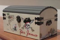 "Small wood Pirate/Treasure Chest... Great for children's play and for storing trinkets and valuables. The chest is light weight and has tiny handles and hardware to accent the corners as well as a felt bottom to protect furniture from being scratched. The inside is decoupaged fabric with Pirates of the Caribbean theme. It may be personalized at no additional cost to you. When ordering please, give the child's name that you wish to have painted on the chest. Dimensions: 9\"X 5\"X 4.72\" *This is