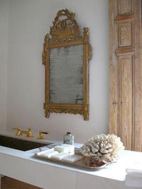 Chic French bathroom features a gold ornate mirror over a floating marble vanity fitted with a mosaic tiled sink and polished brass faucet next to a sterling silver tray lined with beautiful soaps.