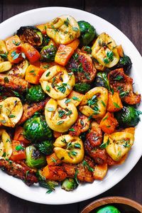 seared chicken, tortellini with roasted butternut squash and brussels sprouts on a white plate