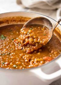 Close up of ladle scooping up Lentil Soup from a white pot, fresh off the stove