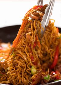 Tongs tossing Chicken Vegetable Ramen Noodles in a black skillet