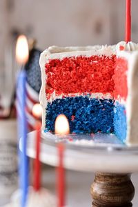 A fun and easy cake decorating project for a red, white and blue cake. This cute holiday cake features two layers of red and blue vanilla cake, frosted with fluffy white buttercream. Red, white and blue sprinkles and birthday candles are all the decoration it needs. Make this festive and colorful cake for the 4th of July or Memorial Day!