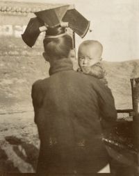 600770.  A Manchu woman wearing elaborate headgear carries a baby.