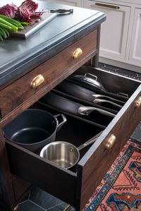 This custom island features several storage ideas. A produce drawer keeps potatoes, onions, and other veggies out of sight and fresh thanks to the mesh door front. A clever spot for pots and pans keeps lids and pans together, organized, and easily accessible. While another drawer with pegs that can be easily arranged keep dishes in order. 