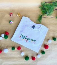 Christmas Lights T-shirt // Holiday Gift for Friend // Hand Embroidered Christmas Shirt A simple string of multicolored lights hand embroidered on a White or Black T-shirt. No matter what holiday you celebrate, these tees can bring some winter magic into your wardrobe this season! Perfect holiday gift for friend or collect matching Christmas shirts for your family. Wear this embroidered tee to your holiday events or Christmas parties.  JackRabbitCrafts Makes Hand Embroidered T-Shirts Made to Ord