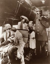 1909. A group of passengers and conductor on a passenger train car.