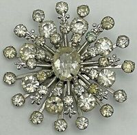 Great looking shape also resembles a flower or starburst form. Classic snowflake shape is decorated with different size rhinestones and accented with tiny fleur-de-lis accents. Overall GOOD condition for its age.