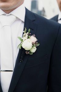 Groom wearing navy suit with white tie, silver tie bar and white rose boutonniere |