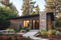 A gently rising roofline from left to right, vertical siding and a stone fireplace give this 938 square foot house a contemporary vibe and makes it suitable in the woods or out in the open. Inside, two bedrooms with 9' ceilings line the left side of the  home and are separated by a bathroom giving you extra privacy. The right side of the plan has ceilings that slope left-to-right and gives you a front-to-back open space. The living room with fireplace is in front. The kitchen has an island