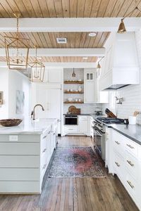 A red and black vintage rug sits on a thin plank floor accenting an expansive white kitchen.