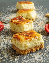 Four Creme Brulee Cheesecake Bars arranged in a line with a sprinkling of sugar.