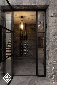 This wine cellar room blends rustic charm with luxury, featuring walnut cabinetry, custom wine racks, and generous counter space for wine prep and serving. Elegant black-framed glass doors and a striking stone wall complete the look. #WineRoomDesign #LuxuryWineRoom #WineStorageSolutions #WineDisplay #WineRoomInspiration