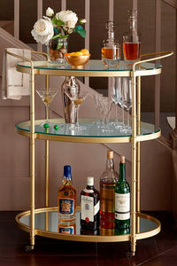 The Estelle Bar Cart serves up sophisticated splendor. This three-tier serving cart has a metal frame with a gold finish, two glass shelves, and an antique mirrored shelf on the bottom. 