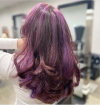 Layered With Purple Highlights In Brown Hair: Layered with purple highlights in brown hair, this style embodies a sophisticated fusion of texture and color, seamlessly blending the depth of layered locks with the allure of strategically placed purple accents. This hairstyle features a cascade of layered brown...