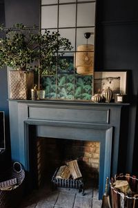 A gorgeous dark and moody, eclectic and glamorous living room design from Fiona Duke interiors with lovely copper framed mirror, botanical, tropical style influences and great fireplace styling.