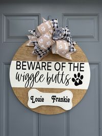 Let everyone know to beware of the wiggle butts in your home. This humorous door hanger is sure to get a smile on the faces of all who sees it. Show off your love for your furry friends. This door hanger is Handmade on an 18" round, 1/2" thick birch plywood. Hand stained and painted. Sealed with a durable topcoat for protection. This Design is made with premium permanent Vinyl. Greenery and bow attached with staples or hot glue. Jute rope attached for hanging. * Message me for personalization of