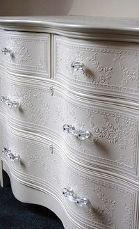 White shabby chic painted dresser with embossed white floral wallpaper on the drawers