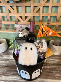 A ghost print bucket with a bottle of wine, 2 plastic stemless tumblers with “Boos” messaging, ghost wine stopper, felt ghost, gel ghost window cling, “Boo Crew” pennant & chocolate ghost truffles. A fun fall themed raffle, auction or fift basket!