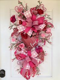 "Your door will be stunning this Valentine's Day dressed with this beautiful festive teardrop swag.  This swag is loaded with pink and red roses, tiny pink wildflowers, and white glittery picks.  Pink and red glittered hearts add to the Valentine's theme of this swag.  The beautiful colors of the multi-ribbon bows and streamers compliment the wooden heart.  This charming Valentine swag would be a show-stopper on anyone's front door.  Ready to ship!   Measurements:  The swag measures 36\" in heig