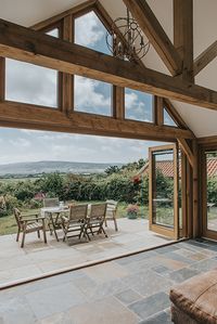 An oak framed extension and outdoor dining area with stunning views #oakwindows #oakframedextension #oakframegardenbuilding #oakframedporch #oakframedorangery