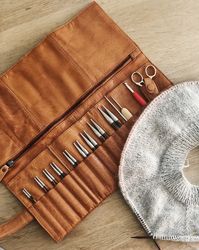 Stockholm is a handmade leather case for interchangeable needles and circulars. Keep your circulars and interchangeable knitting needles perfectly organized with the beautiful Stockholm leather case from muud. This is a must-have accessory for advanced knitters, but the savvy beginner is always welcome to start accessorizing.Handcrafted in premium quality leather that ages with beauty, the Stockholm needle case offers both aesthetics and functionality. The smart design keeps your precious needles in place with a foldover flap. The case has room for 12 sets of interchangeable knitting needles from sizes 2.5 mm – 8 mm. In addition, it features three pockets with room for wires and a large, zipped pocket for additional accessories such as scissors, measuring tape and stitch markers. It is per