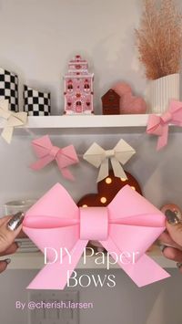 Content Creator: @cherish.larsen As you can see I used this method to make a little garland for my shelves! I made those bows a little bit smaller. These also look super cute on a tablescape, gift box, birthday parties, etc.. These are also easy, easy! If you follow the steps, it’s pretty hard to mess up! *P.S. use cardstock paper for these! They won’t look as cute if you dont! 🎀