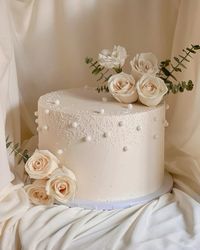 Anniversary cake in white colour theme. Top half of the cake covered with pearl and on the side and top with flower witb little green leaves. 🤍