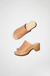 Full coverage clog sandal on mid heel. Neutral, peach-pink leather upper. Open toe. Delicate binding at toe and instep openings. Lightweight, lacquered wood base. Unlined. Domestic clog orders will arrive within 10 business days via UPS Ground. Need it faster? Please call (212) 226-5759 to discuss options and pricing. DETAILS Water repellant cow leather upper. Wood base with polyurethane sole. 2.5" heel with 1" front platform. Handmade in the United States. FIT Ideal for most widths. Leather upp