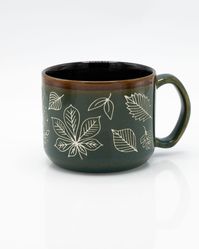 Inspired by the impressions left behind by leaves, the botanical design on this mug is sand-carved by hand for a unique tactile experience.  Give one of these elegant forest green Pressed Leaves mugs to your favorite botanist, dendrologist or significant other and make their day. Each piece is made with care by skilled