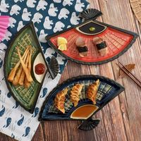 Introducing our exquisite Dumpling Plate with Vinegar Dish, a must-have for any culinary enthusiast. This creative ceramic partition plate is not just a dish, but a piece of art that adds a touch of elegance to your dining table. Hand-painted with intricate details in a Japanese style, this fan-shaped snack plate is perfect for serving sushi, dumplings, or any other delicacies in a unique and stylish way. Crafted from high-quality porcelain, this plate is not only beautiful but also durable and long-lasting. The partition design allows you to separate different types of food while creating a visually appealing presentation. Whether you are hosting a dinner party or simply enjoying a meal at home, this plate will impress your guests and elevate your dining experience. With its sleek and mod