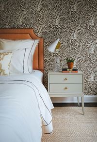 The guest bedroom is cloaked in an Abre de Matisse wallpaper from Quadrille and accented by a natural-fiber rug, Chelsea Editions night table, and modern cone sconce from Circa Lighting | archdigest.com