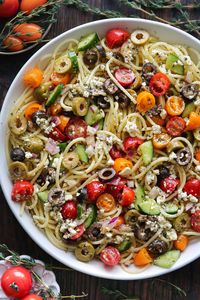 Spaghetti Salad with cherry (or grape) tomatoes, cucumbers, black olives, green olives, red onion, and feta cheese - in a white bowl.