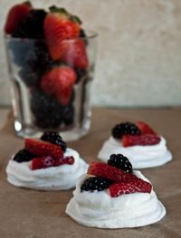 A small batch of mini pavlovas topped with fresh whipped cream and berries.