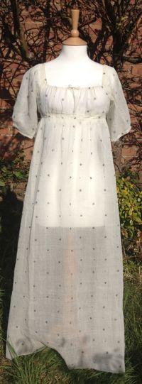 c1805-10 white muslin dress with star and dot design in metallic thread. Short puff sleeves. Back fastening with ties.