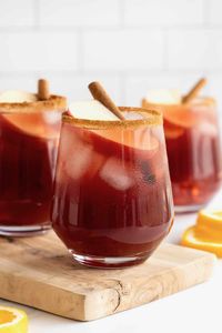 Three glasses of apple cider sangria on a long rectangular wooden cutting board.